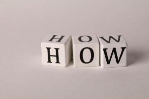 Close-up of white wooden cubes with the letters 'H', 'O', and 'W' arranged on a neutral background.